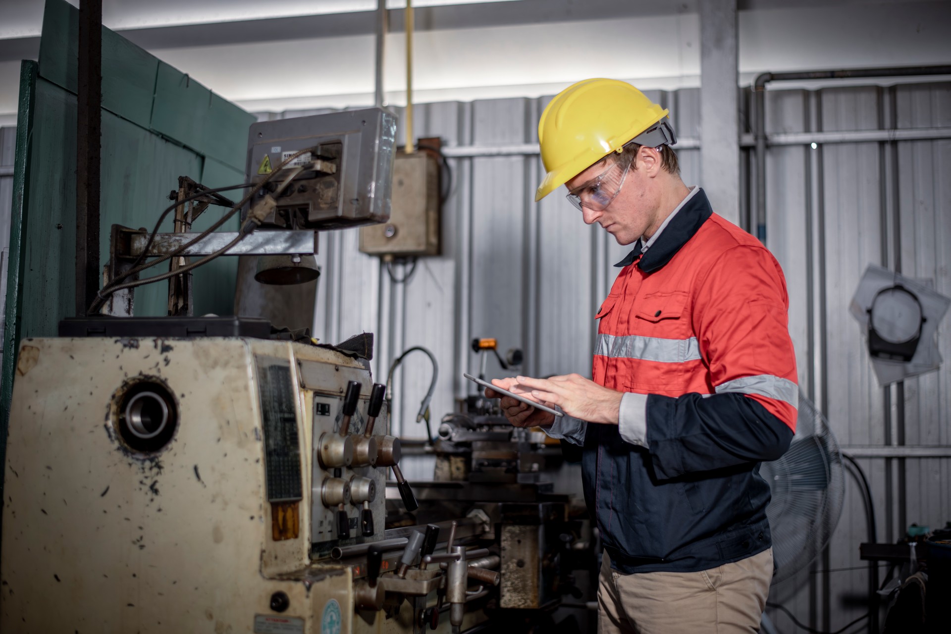 Industry engineer wearing safety uniform control operating lathe grinding machine working with detail tablet computer on hand in industry factory is metal manufacture industry concept.